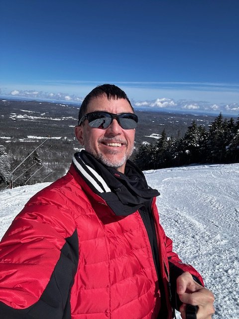 Ken Corriveau smiling on a ski slope in a red jacket